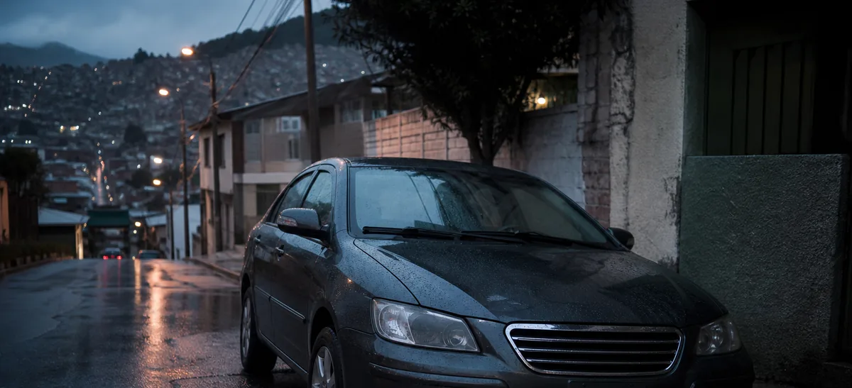Un automóvil sedán aparcado junto al bordillo de una calle residencial mojada en una ciudad andina al atardecer.